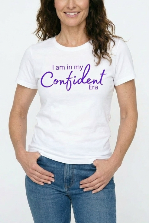 Person wearing a white t-shirt with 'I am in my Confident Era' text on a plain background