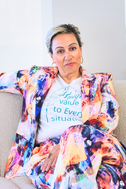 Person wearing a colorful jacket and white t-shirt with text, sitting on a couch.