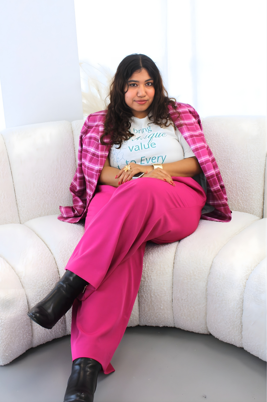 Person sitting on a white couch wearing a pink plaid jacket, white t-shirt, and pink pants.