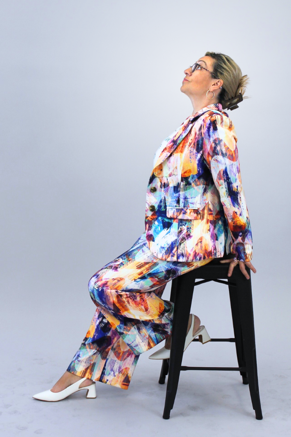 Person wearing a colorful suit sitting on a stool against a plain background