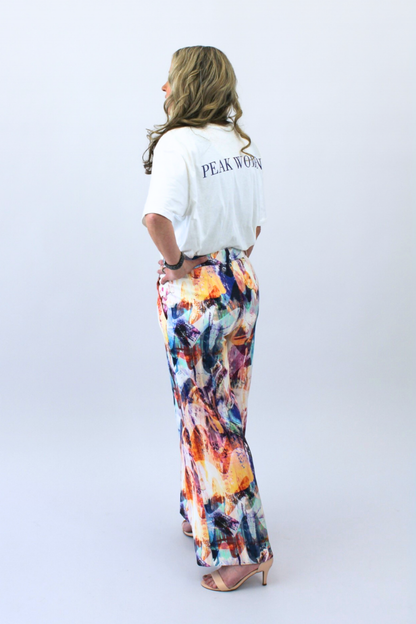 Woman wearing a white shirt with 'PEAK WOMEN' text and colorful pants on a white background