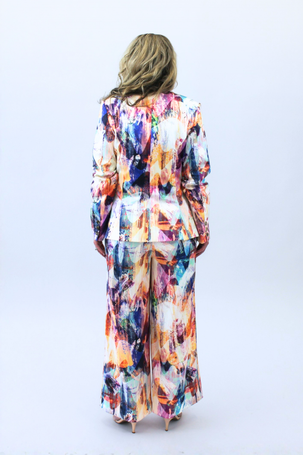 Woman wearing a colorful, patterned outfit on a white background facing backward