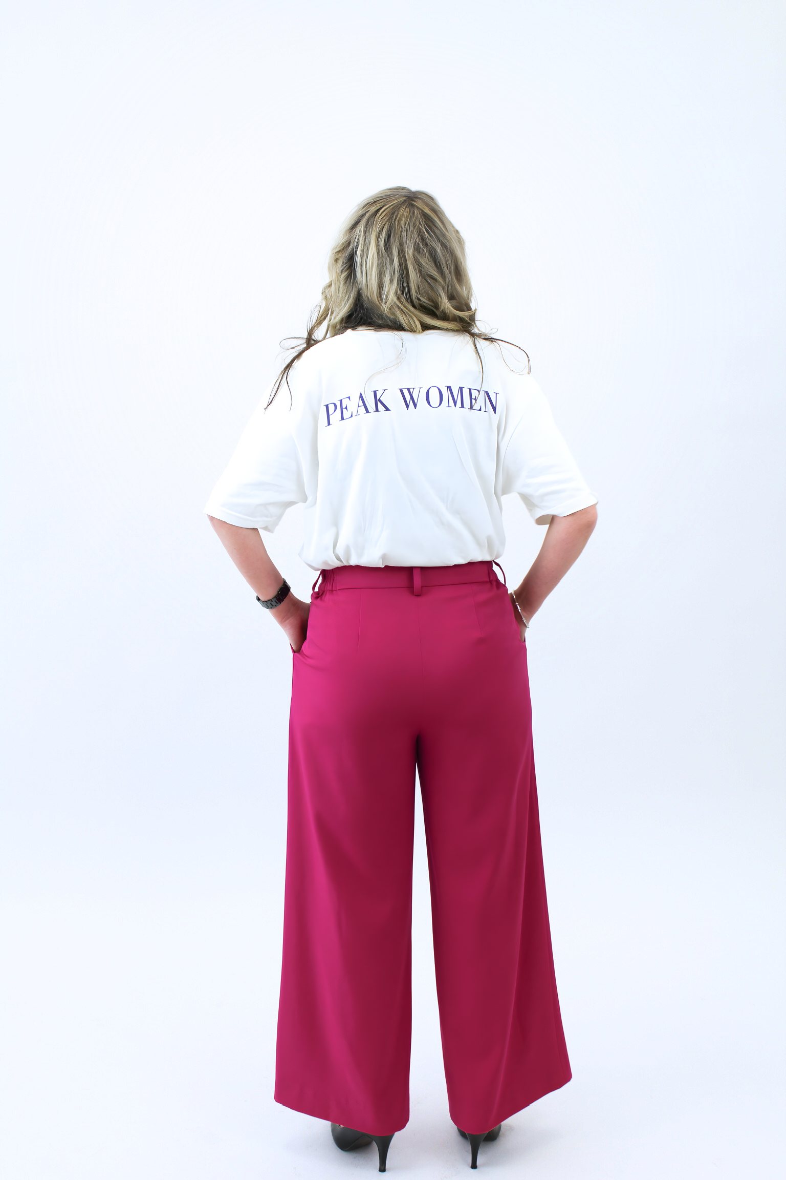 Person wearing a white shirt with 'PEAK WOMEN' text and pink pants on a white background