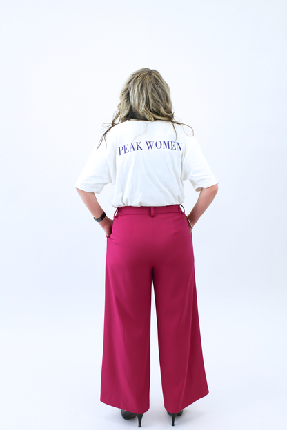 Person wearing a white shirt with 'PEAK WOMEN' text and pink pants on a white background