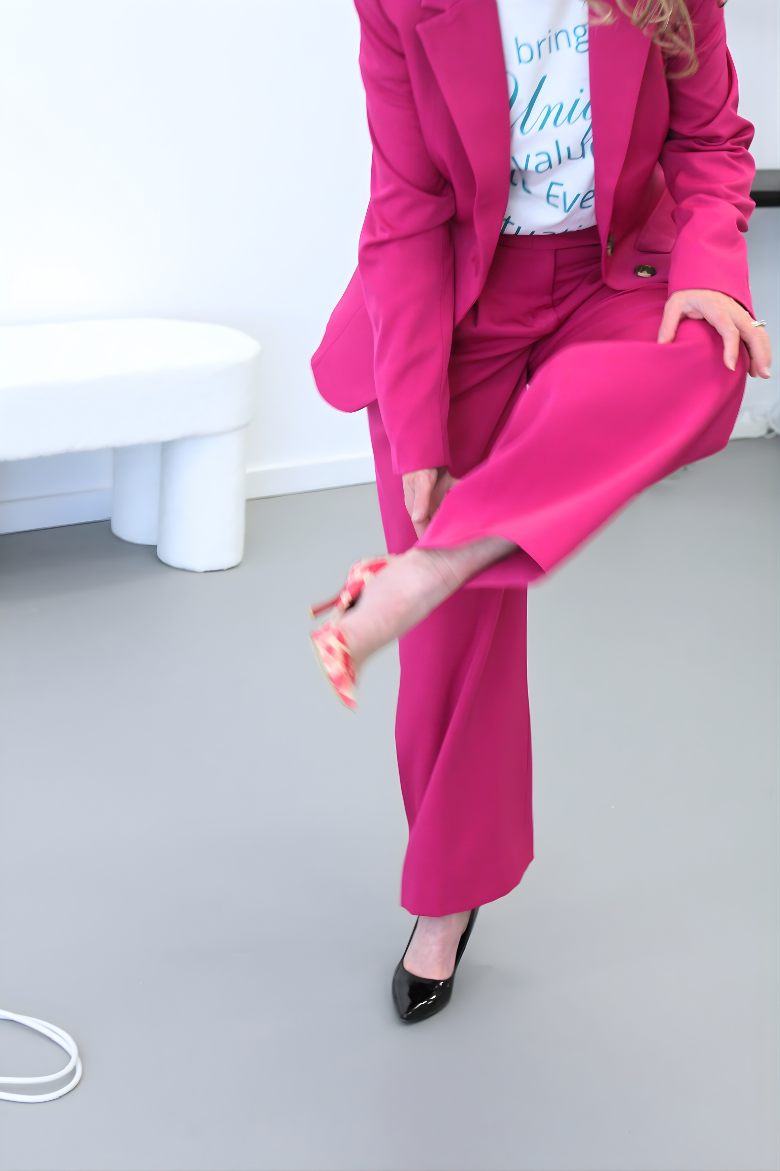 Person wearing a bright pink suit sitting on a white surface.
