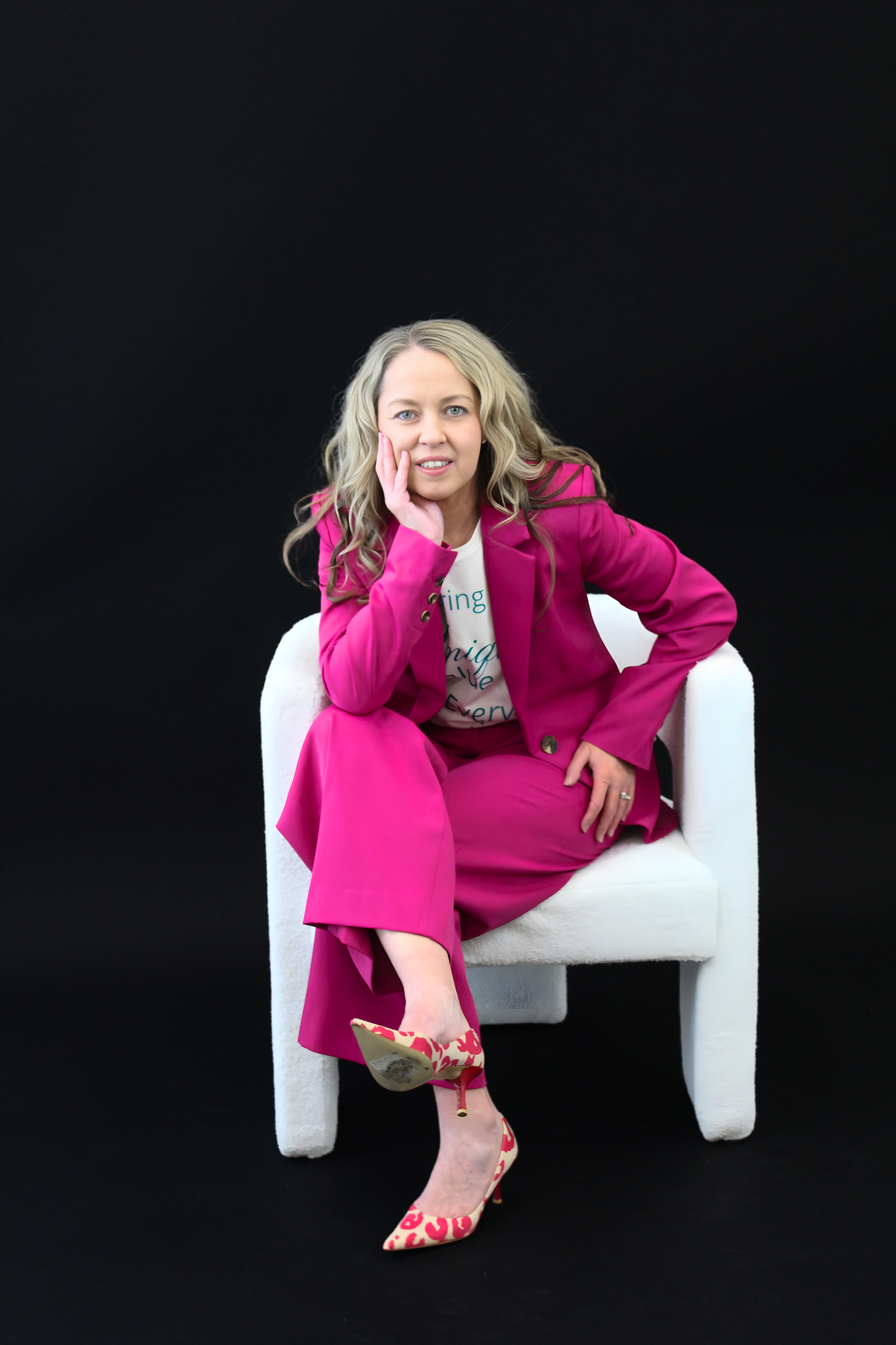 Woman in a bright pink outfit sitting on a white chair against a black background