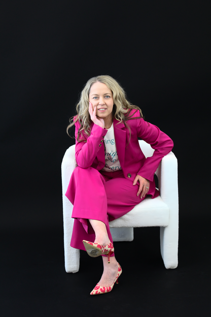 Woman in a bright pink outfit sitting on a white chair against a black background