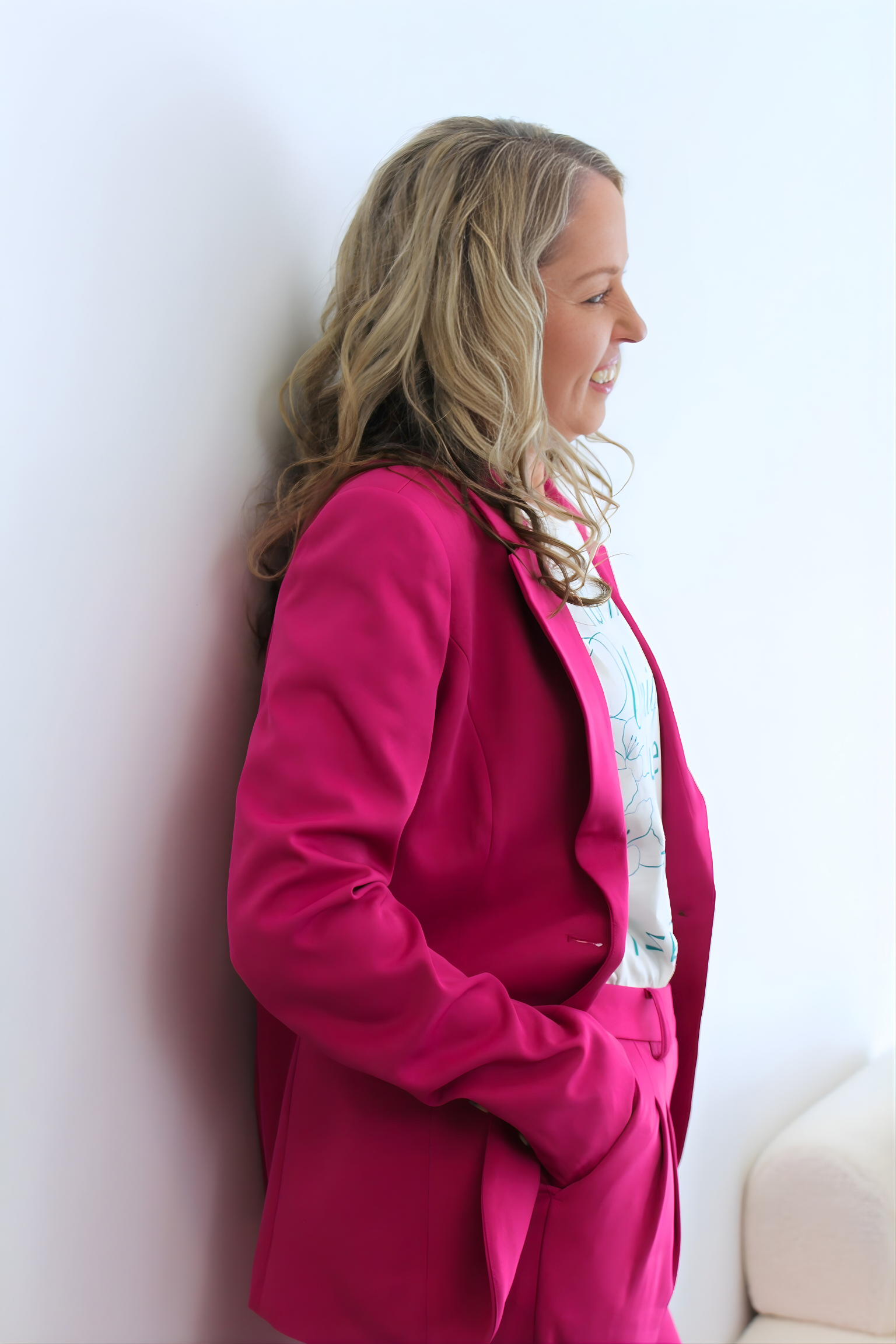 Woman wearing a bright pink coat against a white wall