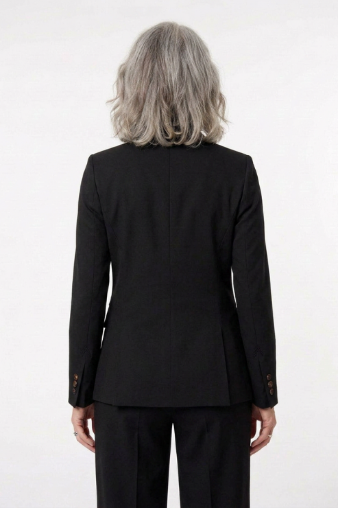 A person viewed from the back wearing a black tailored blazer and black trousers against a plain light background.
