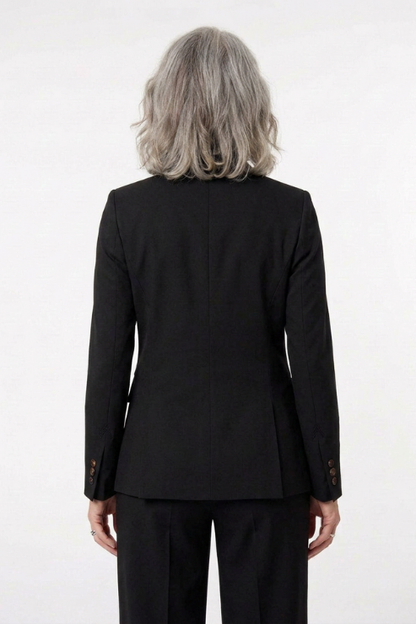 A person viewed from the back wearing a black tailored blazer and black trousers against a plain light background.