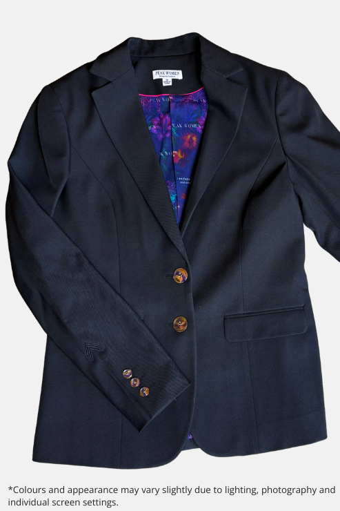 A black blazer jacket with a double-breasted button closure, laid flat on a speckled stone surface. The inner lining is visible and features a purple and blue floral pattern.