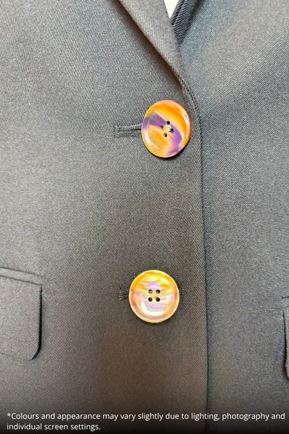 Close-up of a black blazer with two round buttons featuring a marbled orange, yellow, and purple pattern, with a small text disclaimer at the bottom.