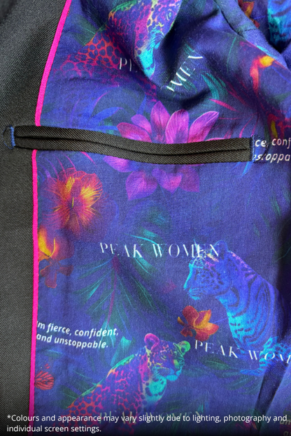 Close-up of a printed garment or fabric panel with a dark zipper and bright pink piping. The print features colorful floral and animal motifs on a deep blue-purple background, with visible text including 'PEAK WOMEN'.