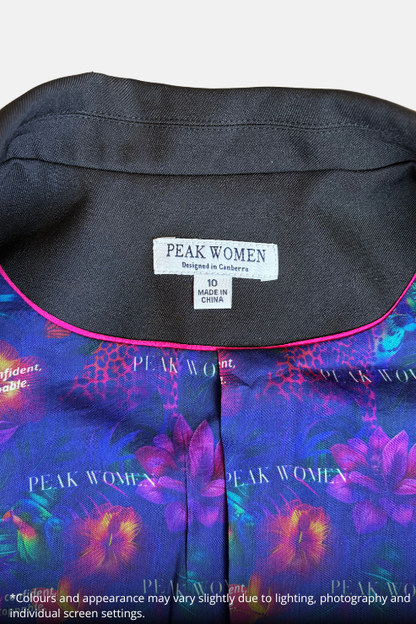 Close-up of a women's blouse collar showing the black neck lining, a white Peak Women brand label, and a colorful floral print in purple, blue, and pink on the fabric.