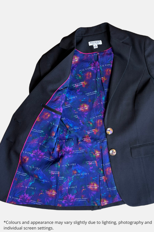 A black blazer jacket laid flat on a speckled stone surface, showing a highly colorful, patterned inner lining with blue, purple, and orange tones. The blazer has two gold buttons and is photographed from a top-down angle.