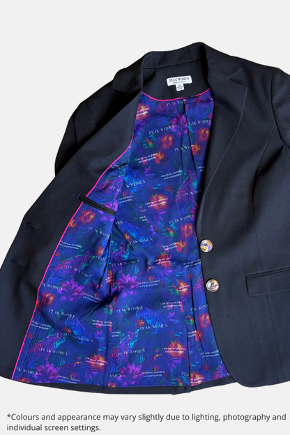 A black blazer jacket laid flat on a speckled stone surface, showing a highly colorful, patterned inner lining with blue, purple, and orange tones. The blazer has two gold buttons and is photographed from a top-down angle.