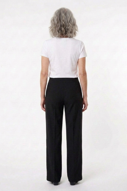 A woman with shoulder-length gray hair is shown from the back, wearing a white short-sleeve crop top and black straight-leg trousers against a plain white studio background.