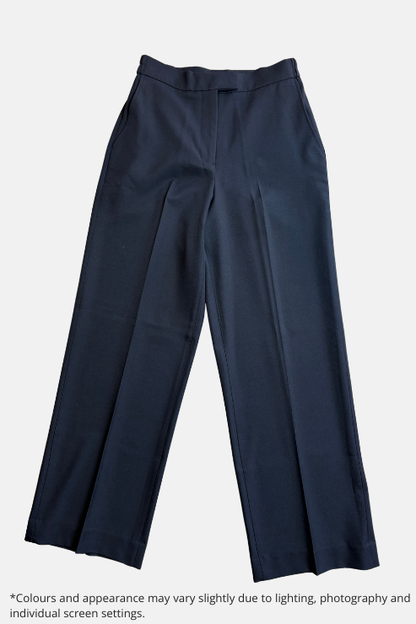 A pair of black tailored trousers laid flat on a speckled light gray floor. The trousers feature a straight, slightly relaxed leg, a clean waistband, and front creases.