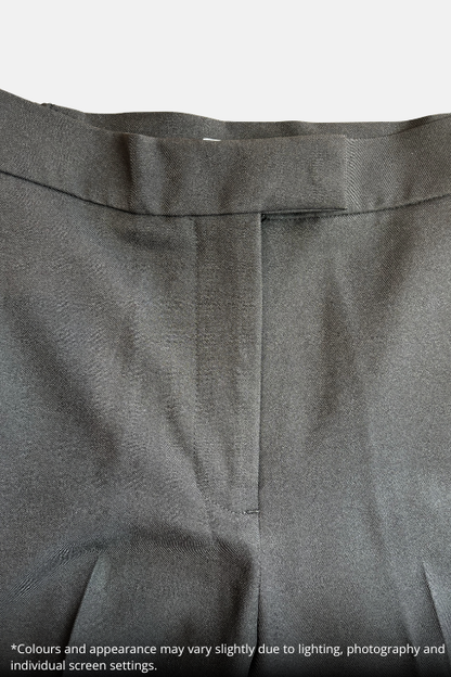 Close-up of a black trousers showing the waistband, belt loops, and front center seam, with a speckled beige countertop visible at the top and a small text disclaimer at the bottom.
