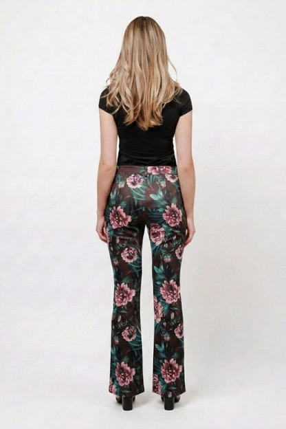 A woman viewed from behind wearing dark floral flare pants with pink flowers and green leaves, paired with a black short-sleeve top, against a plain white studio background.