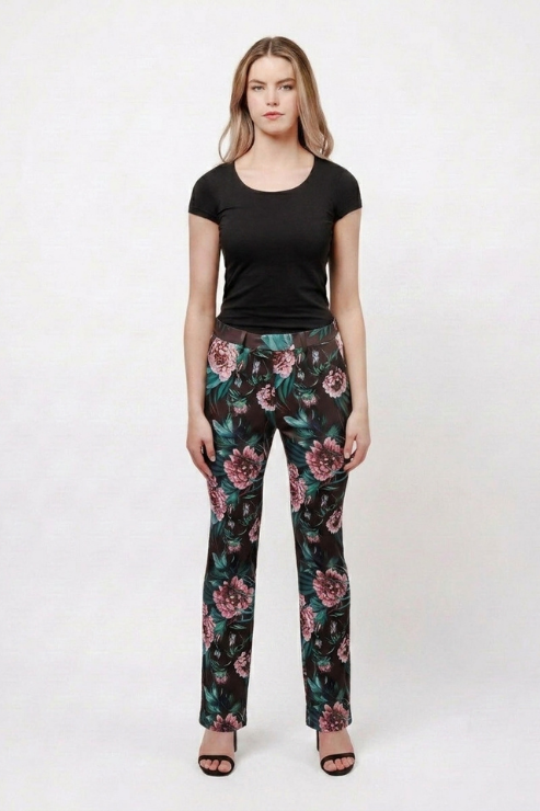 A woman modeling a pair of black straight-leg pants with a pink and green floral print, paired with a black short-sleeve t-shirt and black sandals, against a plain white studio background.