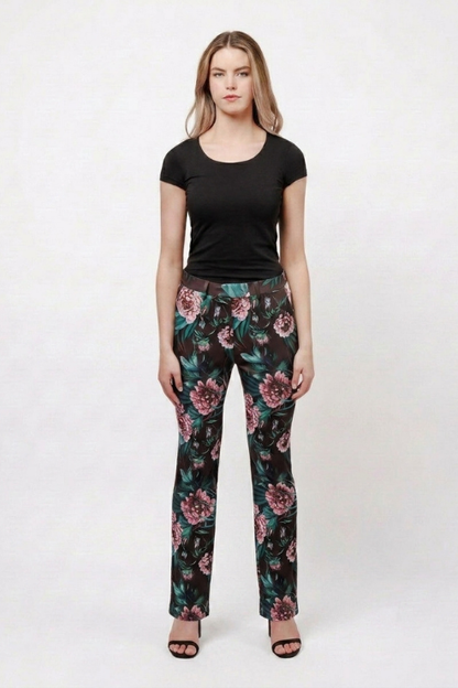 A woman modeling a pair of black straight-leg pants with a pink and green floral print, paired with a black short-sleeve t-shirt and black sandals, against a plain white studio background.