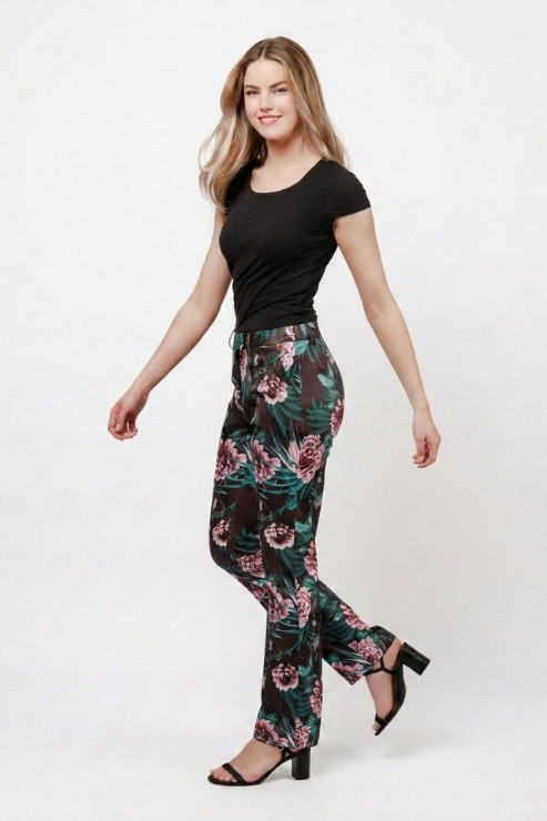 A woman modeling high-waisted floral pants with a black t-shirt and black heeled sandals, standing against a plain white studio background.