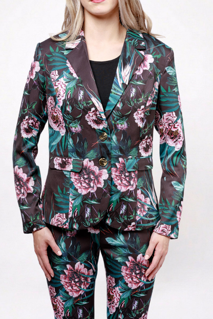 A model wearing a matching two-piece suit featuring a dark brown base with a vibrant pink and green floral print, styled with a black top underneath.
