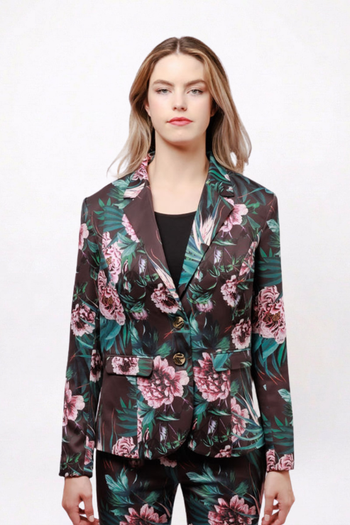 A woman modeling a dark brown floral blazer with pink flowers and green leaves, paired with matching floral pants, against a plain white background.