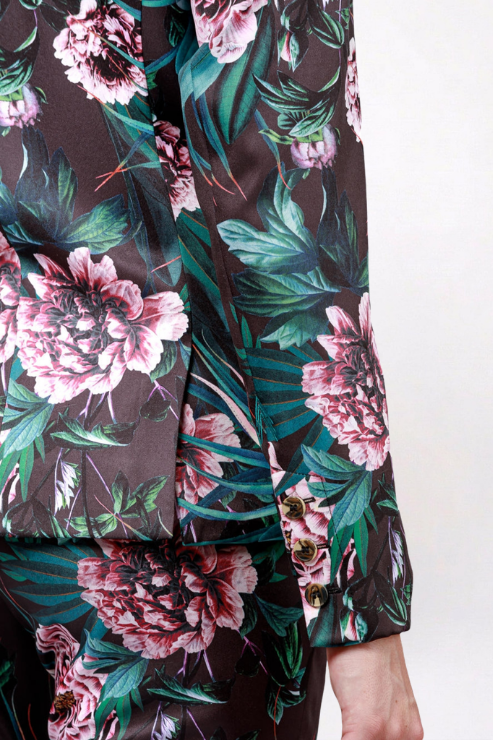 Close-up of a floral-patterned garment with large pink flowers and green leaves on a dark background, shown on a person against a plain light wall.