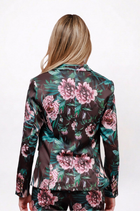 A woman viewed from behind wearing a dark brown satin blazer with a large pink floral print and green leaves, paired with matching pants, against a plain white background.