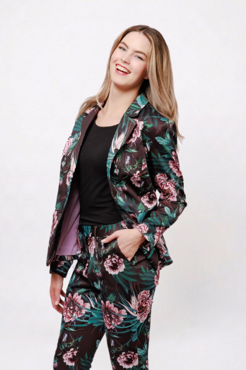 A woman modeling a matching floral print blazer and trousers set with a black top, posing against a plain white studio background.