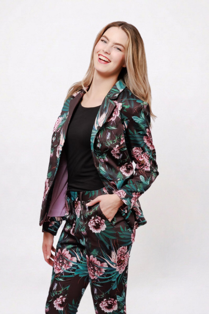A woman modeling a matching floral print blazer and trousers set with a black top, posing against a plain white studio background.