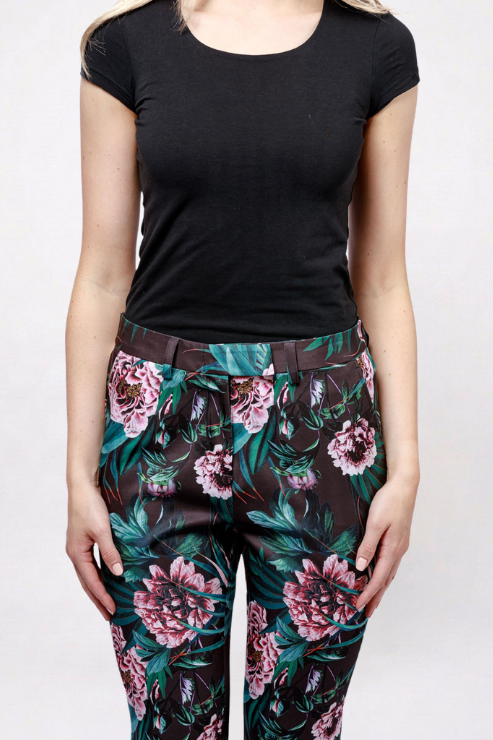 A model wearing a black short-sleeve t-shirt and high-waisted black trousers featuring a vibrant pink and green floral print, paired with a matching floral belt.