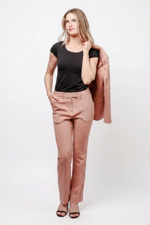 A woman modeling a black short-sleeve t-shirt, dusty rose tailored trousers, and a matching dusty rose blazer draped over her shoulder, set against a plain white studio background.