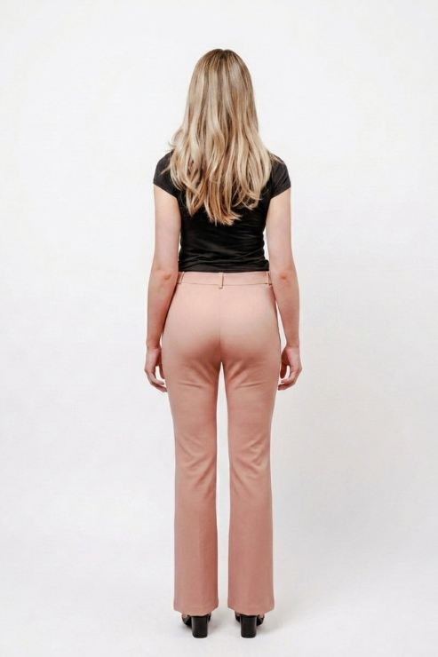 A woman viewed from behind wearing high-waisted blush pink flared trousers, a black short-sleeve top, and black heels against a plain white studio background.
