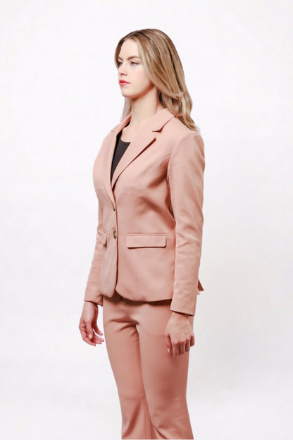 A woman modeling a matching dusty pink blazer and trouser suit, paired with a black top underneath, against a plain white studio background.