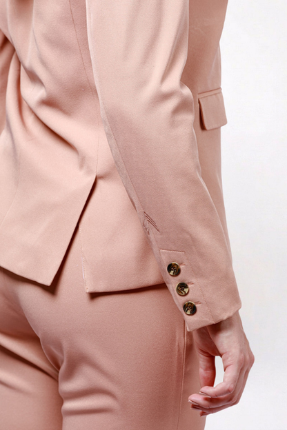 A close-up of a model wearing a light pink tailored suit, showing the back of the jacket with three gold buttons on the sleeve cuff and matching trousers.