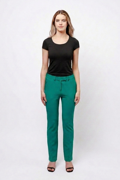 A woman modeling a pair of slim-fit emerald green trousers with a matching belt, paired with a black short-sleeve t-shirt and black sandals, against a plain white studio background.