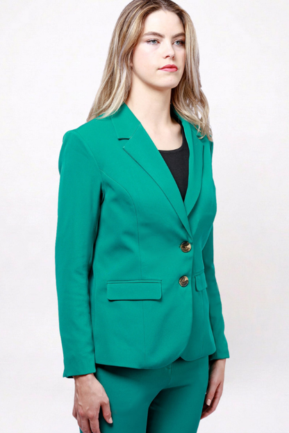 A woman modeling a tailored emerald green blazer with two gold-tone buttons, paired with matching green trousers and a black top, against a plain white studio background.