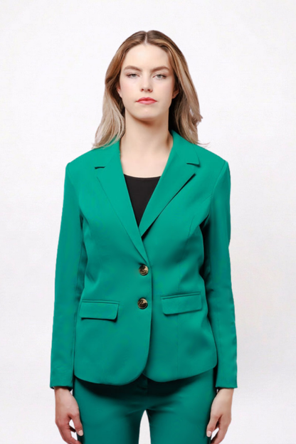 A woman modeling a bright emerald green tailored blazer with notched lapels and two gold-tone buttons, paired with matching green trousers and a black top, against a plain white studio background.
