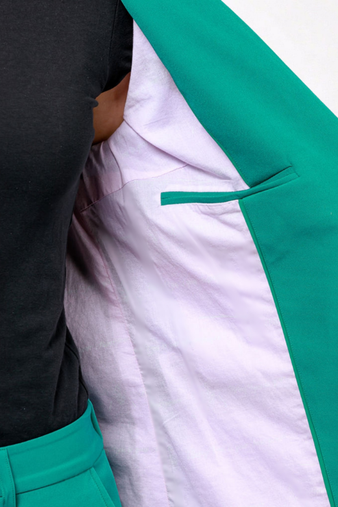 Close-up of a person wearing a bright green blazer over a white shirt and black top, with the blazer open to show the lining and a matching green pocket detail.