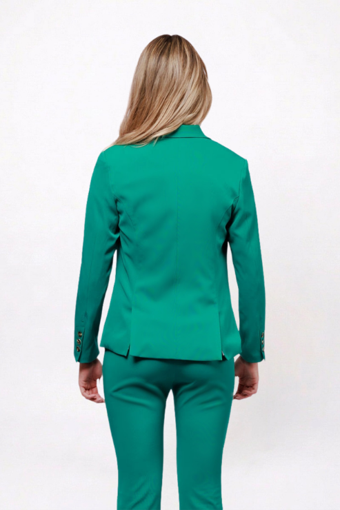 A woman viewed from the back wearing a tailored emerald green blazer and matching trousers against a plain white studio background.
