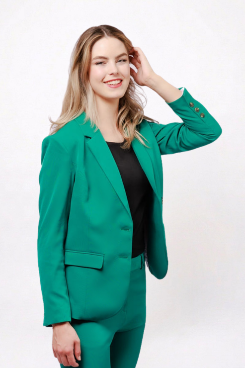 A woman modeling a bright emerald green tailored blazer and matching trousers over a black top, photographed against a clean white studio background.