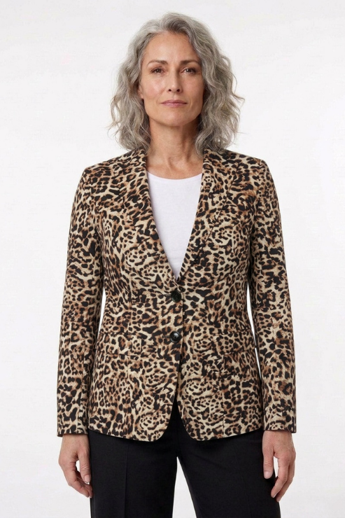 A woman with gray hair wearing a leopard print blazer over a white top and black pants, standing against a plain white studio background.