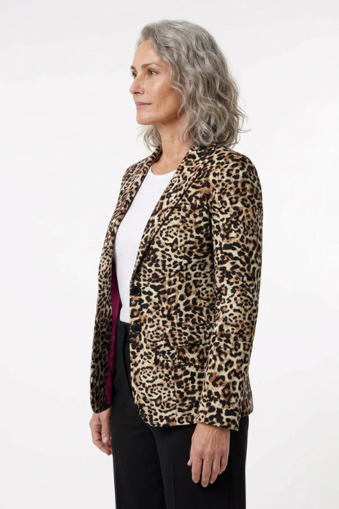 A woman with gray hair is shown in profile wearing a leopard print blazer over a white top and black trousers, photographed against a plain white studio background.