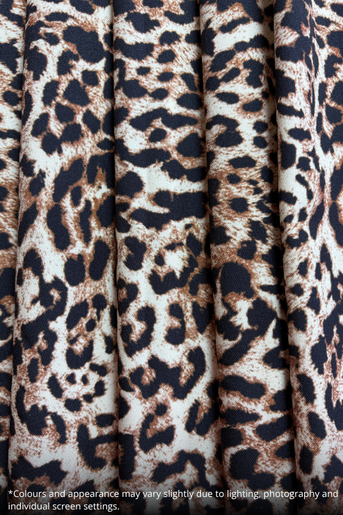 Close-up of a leopard print fabric with vertical pleats, featuring a pattern of dark brown, black, and beige spots on a cream background.