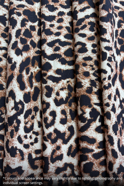 Close-up of a leopard print fabric with vertical pleats, featuring a pattern of dark brown, black, and beige spots on a cream background.