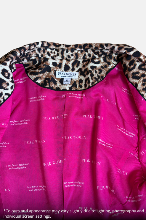 A close-up of a women's top by Peak Women, featuring a vibrant magenta pink satin-like fabric printed with the brand name, layered over a leopard print lining.