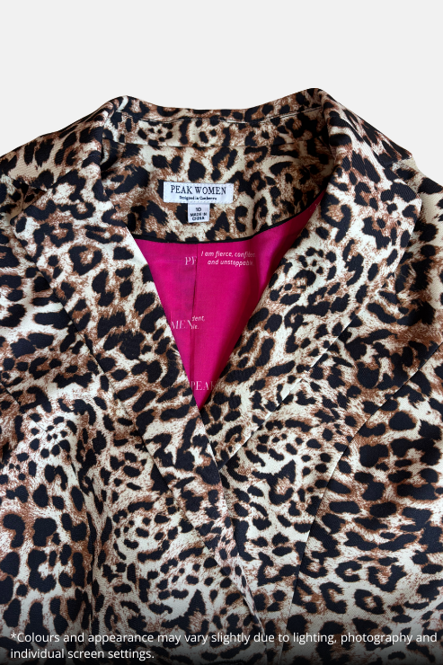 Close-up of a leopard print top by Peak Women, featuring a beige, brown, and black animal pattern with a vibrant hot pink inner lining visible at the collar.